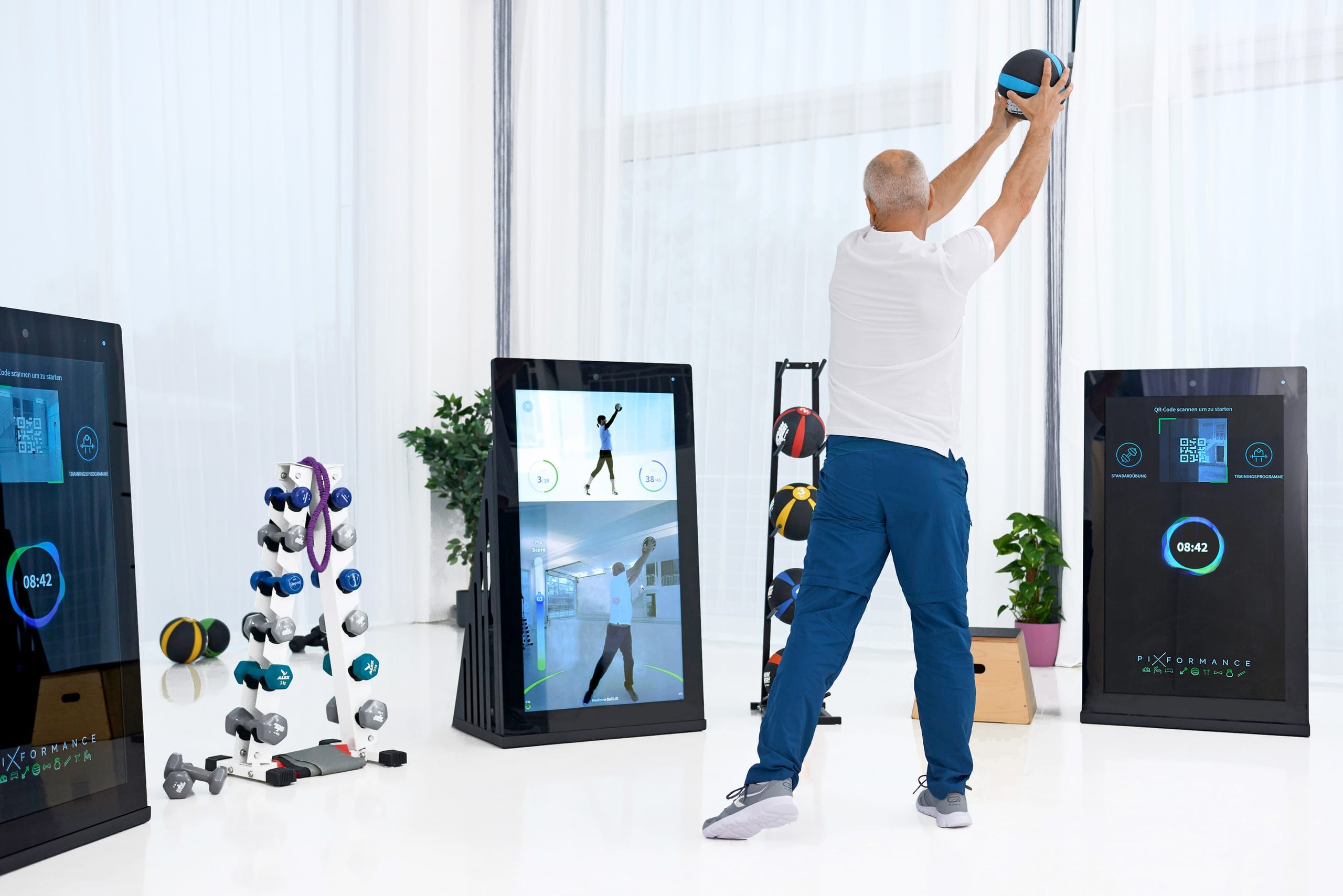 A man training with a medicine ball in front of a Pixformance Station, which shows his movement on screen